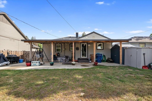 back of property with an outbuilding, a patio, a storage unit, a lawn, and fence