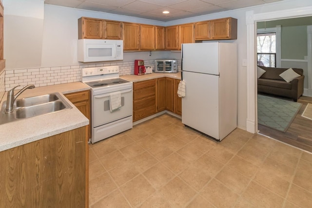 kitchen with brown cabinets, light countertops, backsplash, a sink, and white appliances