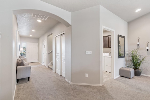 hallway featuring visible vents, arched walkways, washing machine and clothes dryer, a textured ceiling, and carpet flooring