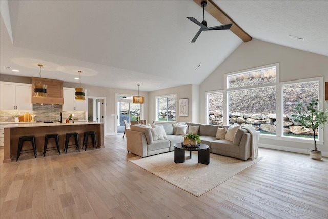 living room with baseboards, light wood-style flooring, ceiling fan, high vaulted ceiling, and beam ceiling