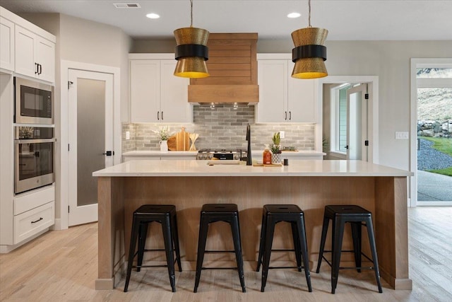 kitchen with built in microwave, backsplash, white cabinetry, light wood-type flooring, and oven