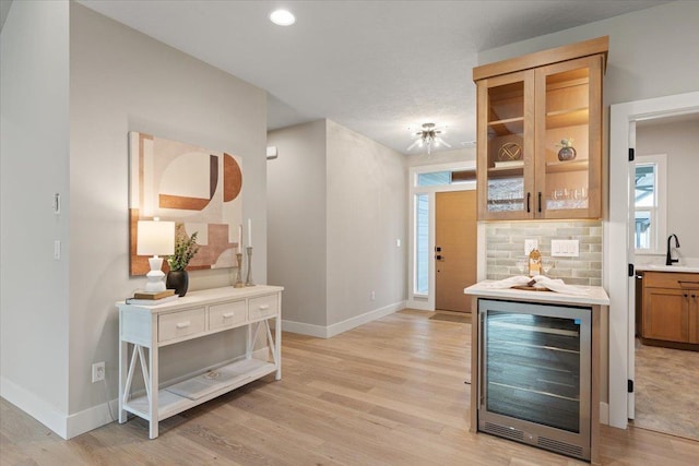 kitchen featuring wine cooler, decorative backsplash, light wood-style floors, a sink, and baseboards