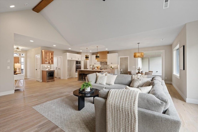 living area featuring high vaulted ceiling, wine cooler, visible vents, light wood-type flooring, and beamed ceiling