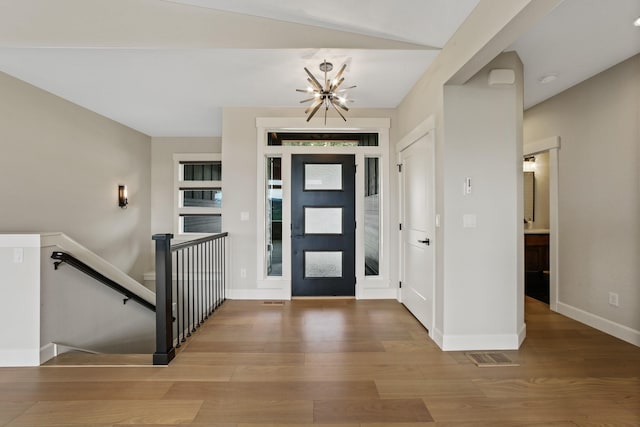 foyer entrance with a chandelier, wood finished floors, visible vents, and baseboards