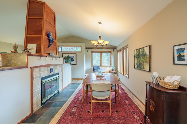 dining room featuring baseboards, a chandelier, vaulted ceiling, and a tiled fireplace