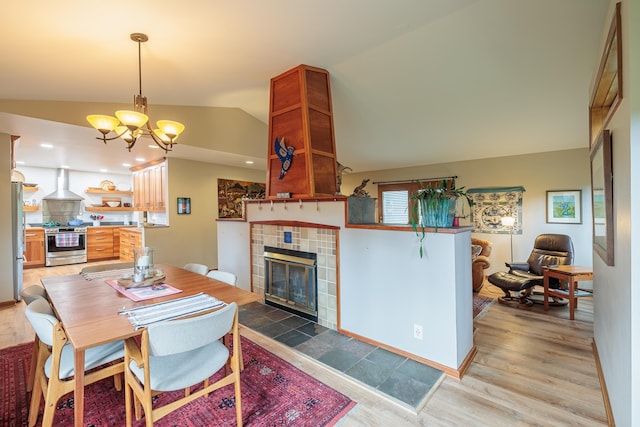 dining room with a chandelier, light wood-type flooring, a fireplace, and vaulted ceiling