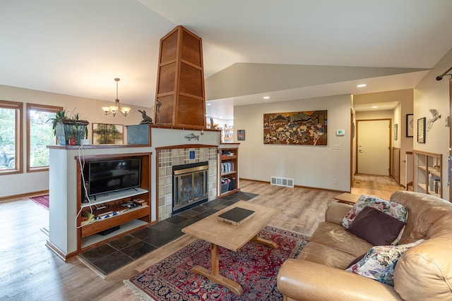 living room featuring a fireplace, lofted ceiling, visible vents, wood finished floors, and a chandelier