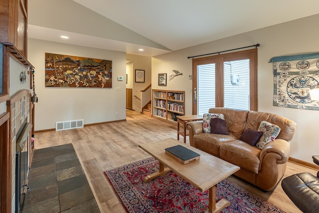 living area with a tile fireplace, wood finished floors, visible vents, baseboards, and vaulted ceiling