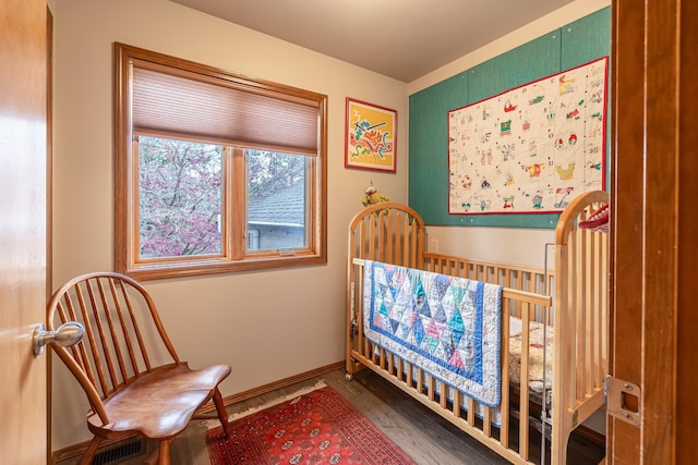 bedroom with a crib, wood finished floors, visible vents, and baseboards