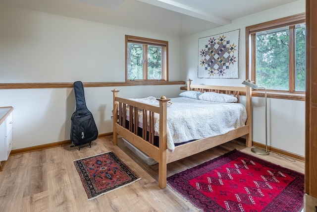 bedroom featuring light wood-type flooring, beamed ceiling, and baseboards