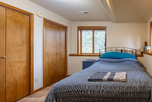 bedroom featuring light wood-type flooring, baseboards, visible vents, and two closets