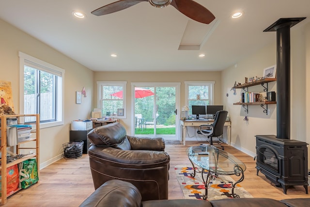 living area with a wood stove, light wood-type flooring, baseboards, and recessed lighting