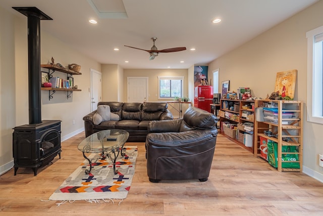 living area with recessed lighting, a ceiling fan, baseboards, light wood-type flooring, and a wood stove