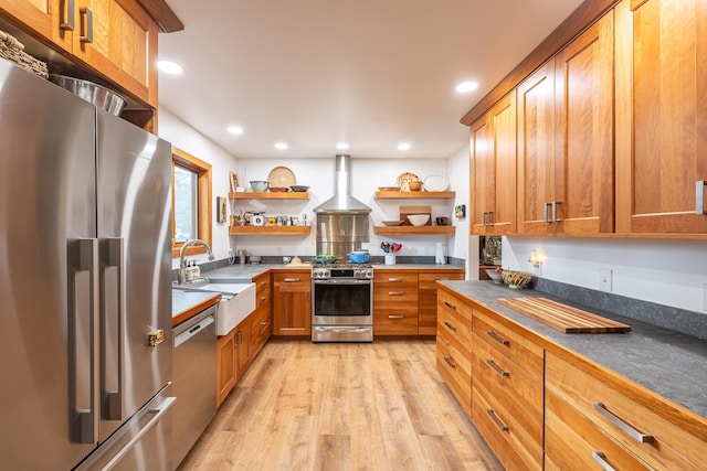 kitchen with light wood finished floors, open shelves, appliances with stainless steel finishes, a sink, and wall chimney range hood