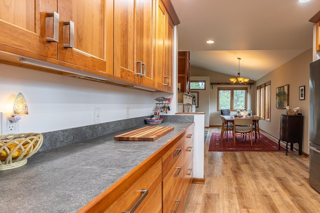 kitchen featuring lofted ceiling, light wood-type flooring, brown cabinets, dark countertops, and an inviting chandelier