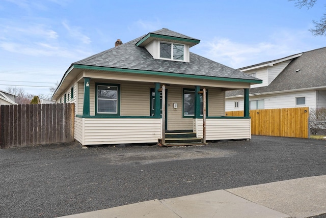 bungalow-style house with driveway, a porch, a shingled roof, and fence