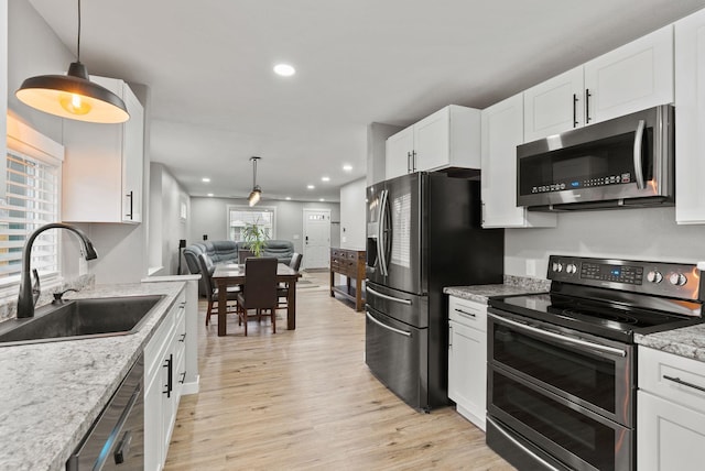 kitchen with light wood-style flooring, appliances with stainless steel finishes, open floor plan, white cabinetry, and a sink