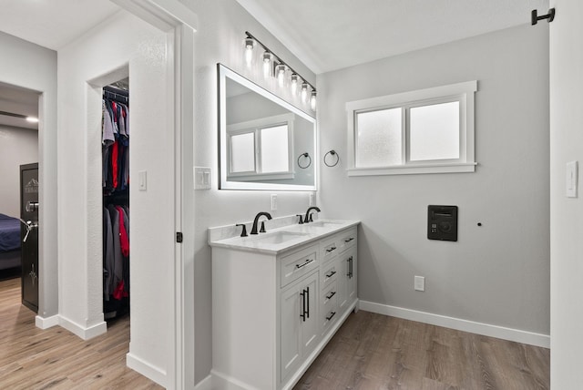 full bath featuring double vanity, a sink, baseboards, and wood finished floors