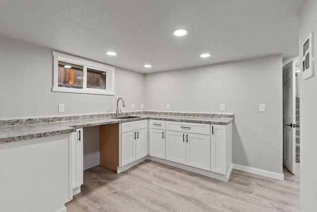 kitchen with light wood finished floors, baseboards, white cabinets, a sink, and recessed lighting