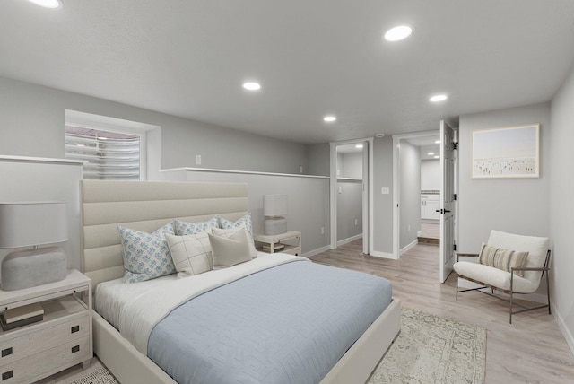 bedroom with light wood-style flooring, baseboards, a walk in closet, and recessed lighting