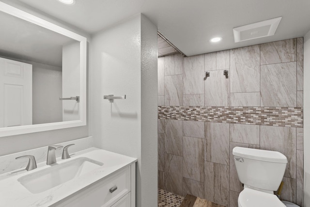 full bathroom with visible vents, toilet, a tile shower, vanity, and recessed lighting