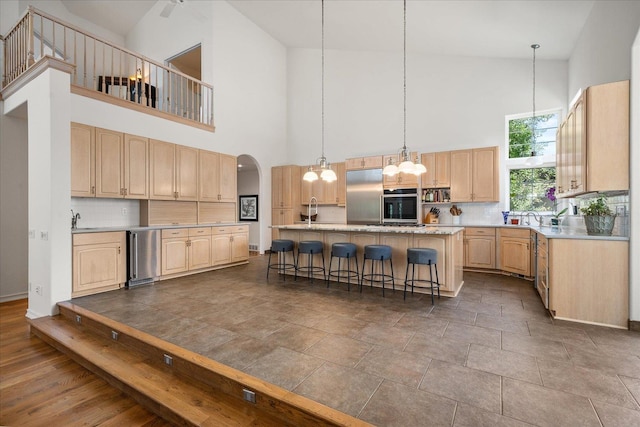 kitchen featuring arched walkways, light brown cabinets, light countertops, tasteful backsplash, and a kitchen bar