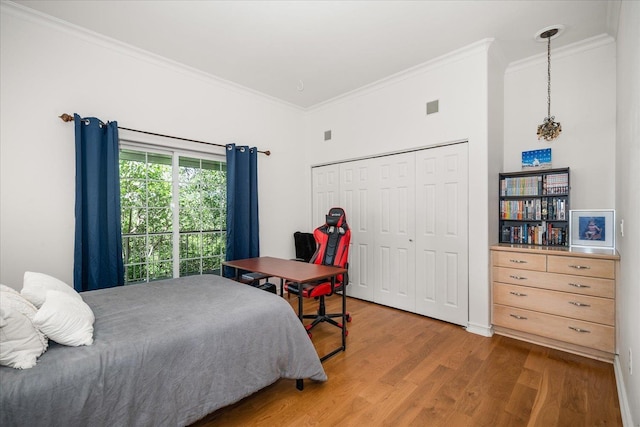 bedroom with a closet, wood finished floors, visible vents, and crown molding