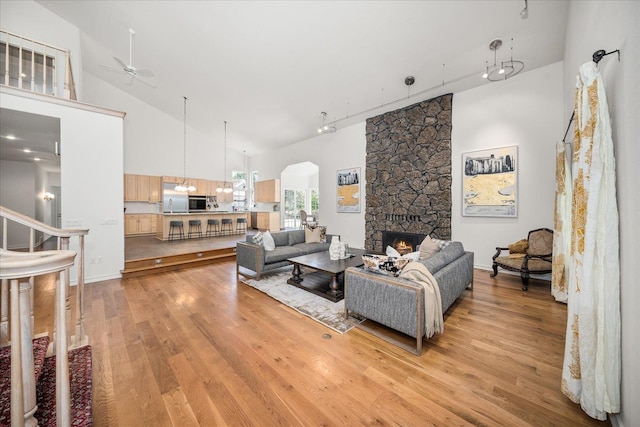 living room with a ceiling fan, light wood-style flooring, stairs, a fireplace, and high vaulted ceiling