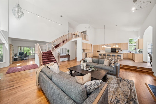 living area with ceiling fan with notable chandelier, high vaulted ceiling, light wood finished floors, and stairway