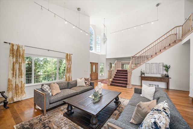 living area with a high ceiling, wood finished floors, baseboards, stairway, and track lighting