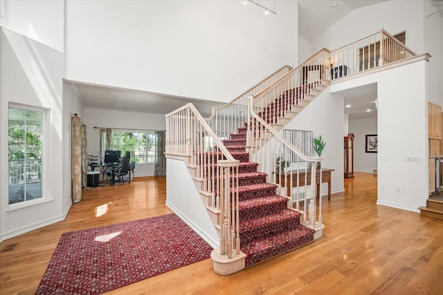 stairway featuring wood finished floors, a towering ceiling, and baseboards