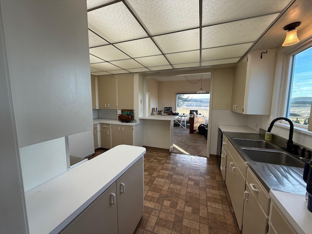 kitchen featuring light countertops, a drop ceiling, a sink, and baseboards