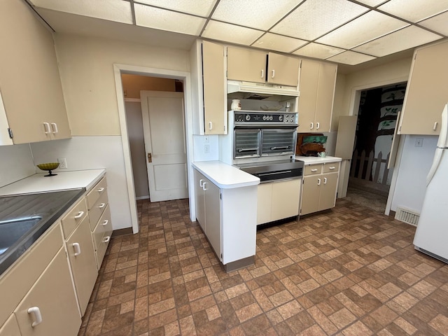 kitchen featuring a drop ceiling, oven, under cabinet range hood, visible vents, and freestanding refrigerator