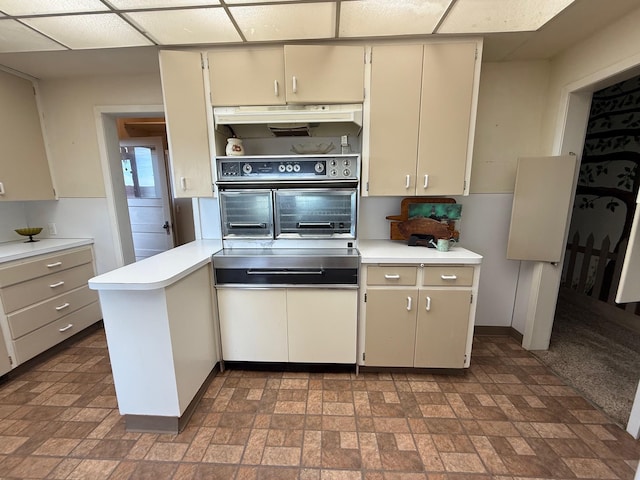 kitchen featuring a paneled ceiling, light countertops, cream cabinets, wall oven, and under cabinet range hood