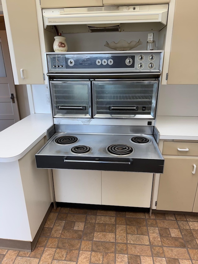 kitchen with brick floor, light countertops, under cabinet range hood, and open shelves