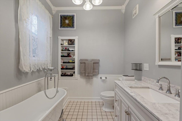 full bath featuring a freestanding bath, ornamental molding, wainscoting, vanity, and tile patterned flooring