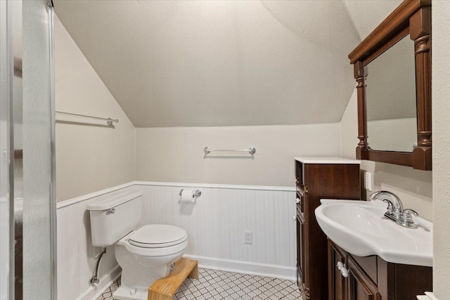 bathroom featuring a wainscoted wall, lofted ceiling, toilet, vanity, and a textured ceiling