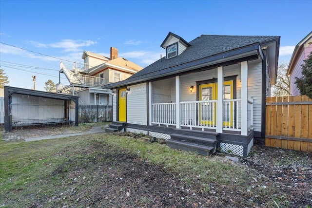 rear view of house with a shingled roof, fence, a porch, and a lawn