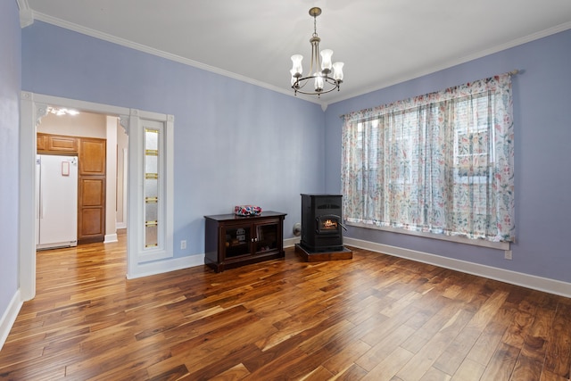 interior space with a notable chandelier, wood finished floors, baseboards, a wood stove, and crown molding