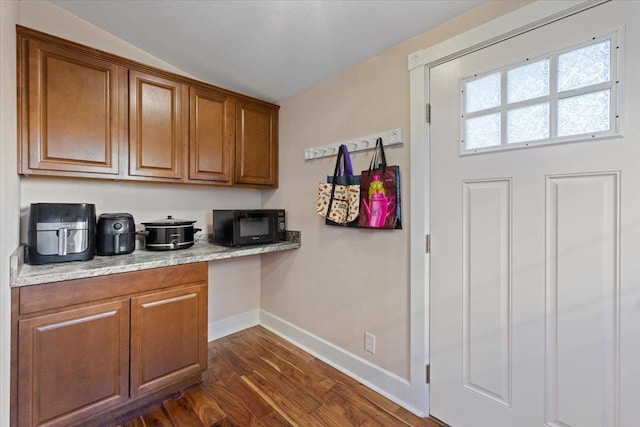 kitchen featuring brown cabinetry, black microwave, dark wood-type flooring, and baseboards