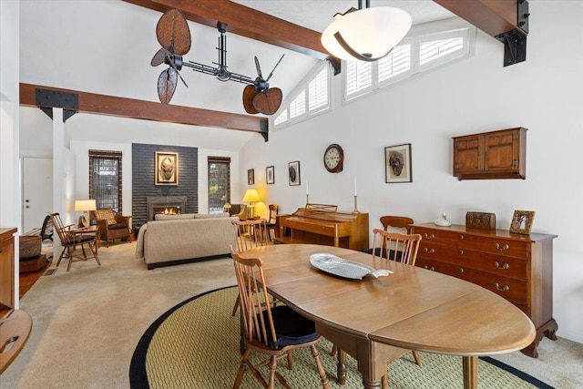 dining room featuring a warm lit fireplace, high vaulted ceiling, beam ceiling, and light colored carpet