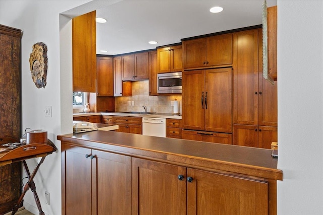 kitchen featuring brown cabinetry, backsplash, built in appliances, a sink, and recessed lighting