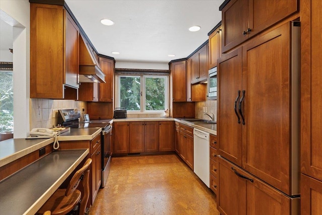 kitchen featuring brown cabinetry, decorative backsplash, stainless steel appliances, light floors, and a sink