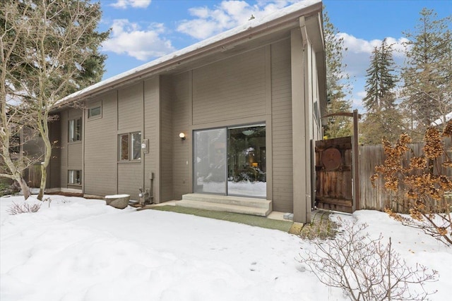 snow covered back of property featuring entry steps and fence