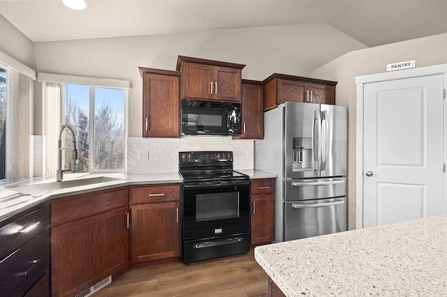 kitchen with decorative backsplash, lofted ceiling, wood finished floors, black appliances, and a sink