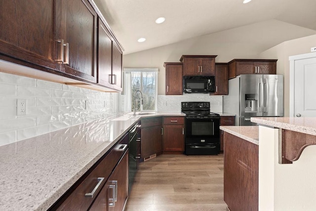 kitchen with light stone counters, light wood finished floors, vaulted ceiling, a sink, and black appliances