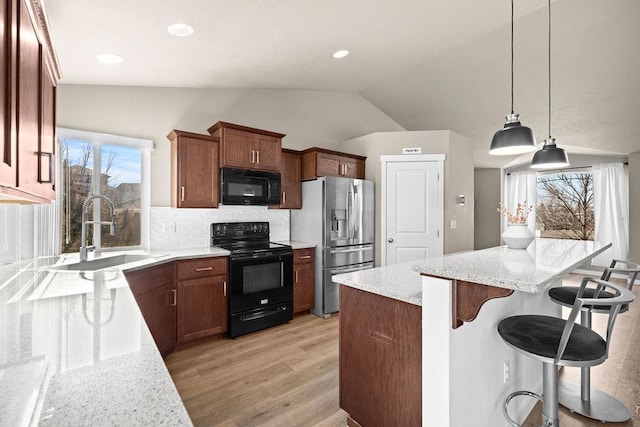 kitchen featuring light stone counters, a breakfast bar, lofted ceiling, a sink, and black appliances