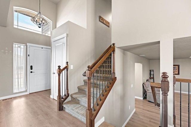 entryway with a chandelier, wood finished floors, a towering ceiling, visible vents, and baseboards