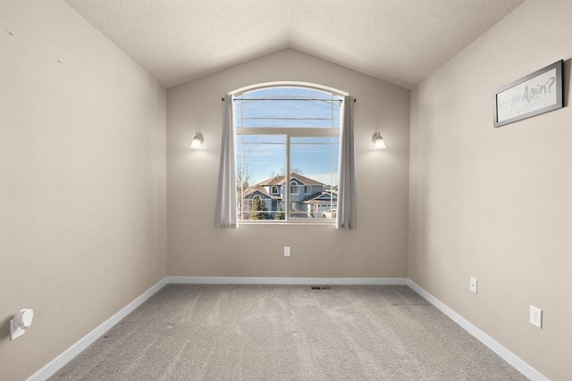 carpeted empty room with lofted ceiling, baseboards, visible vents, and a textured ceiling