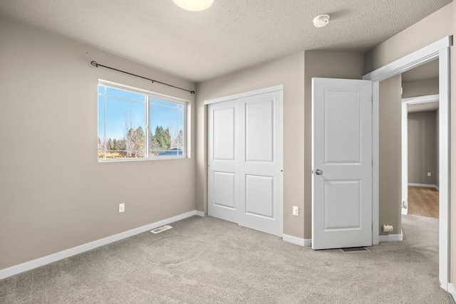 unfurnished bedroom featuring baseboards, visible vents, a textured ceiling, carpet floors, and a closet